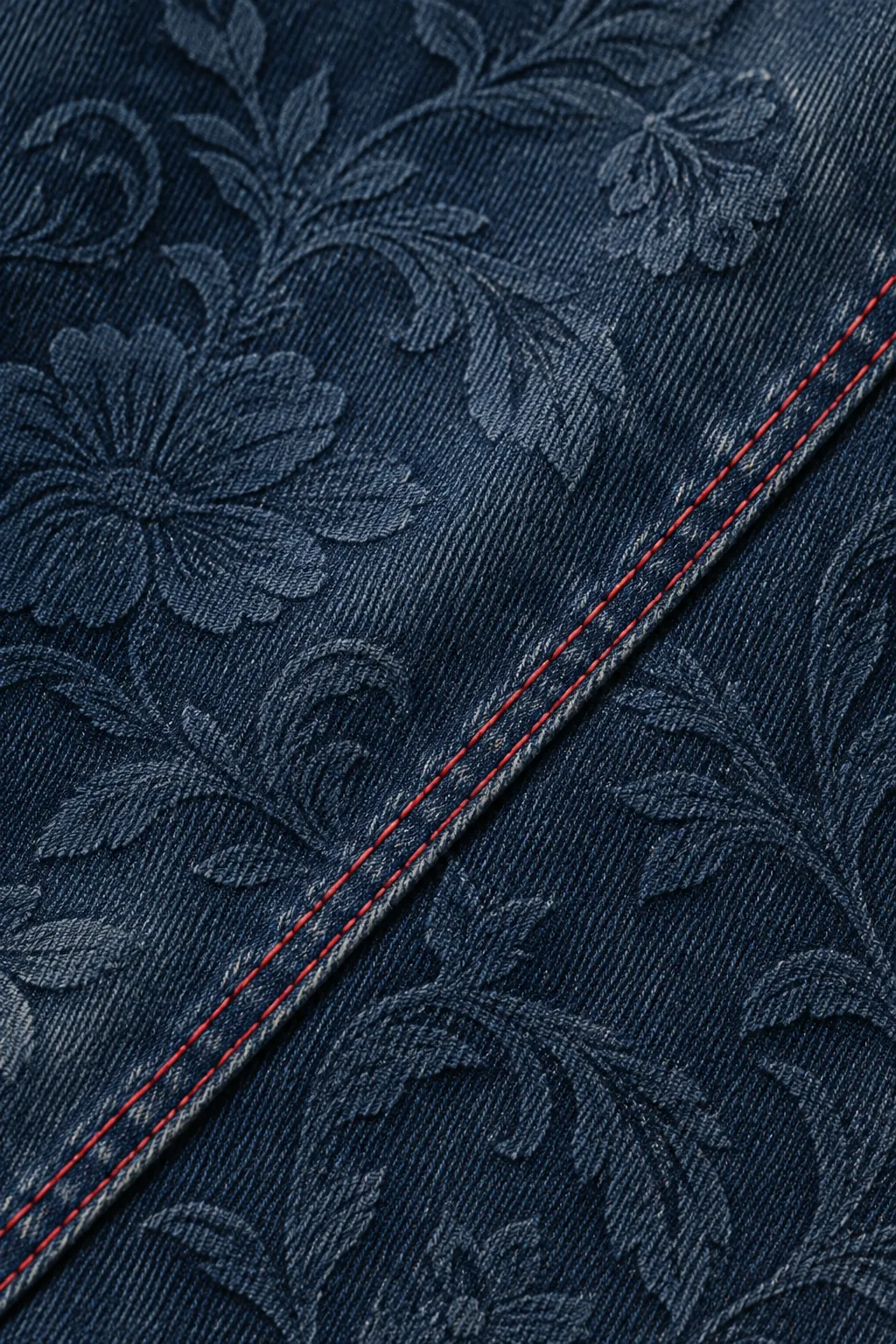 Macro di denim indaco con twill diagonale, stampa in rilievo tono su tono, lavaggio e doppia impuntura rossa.